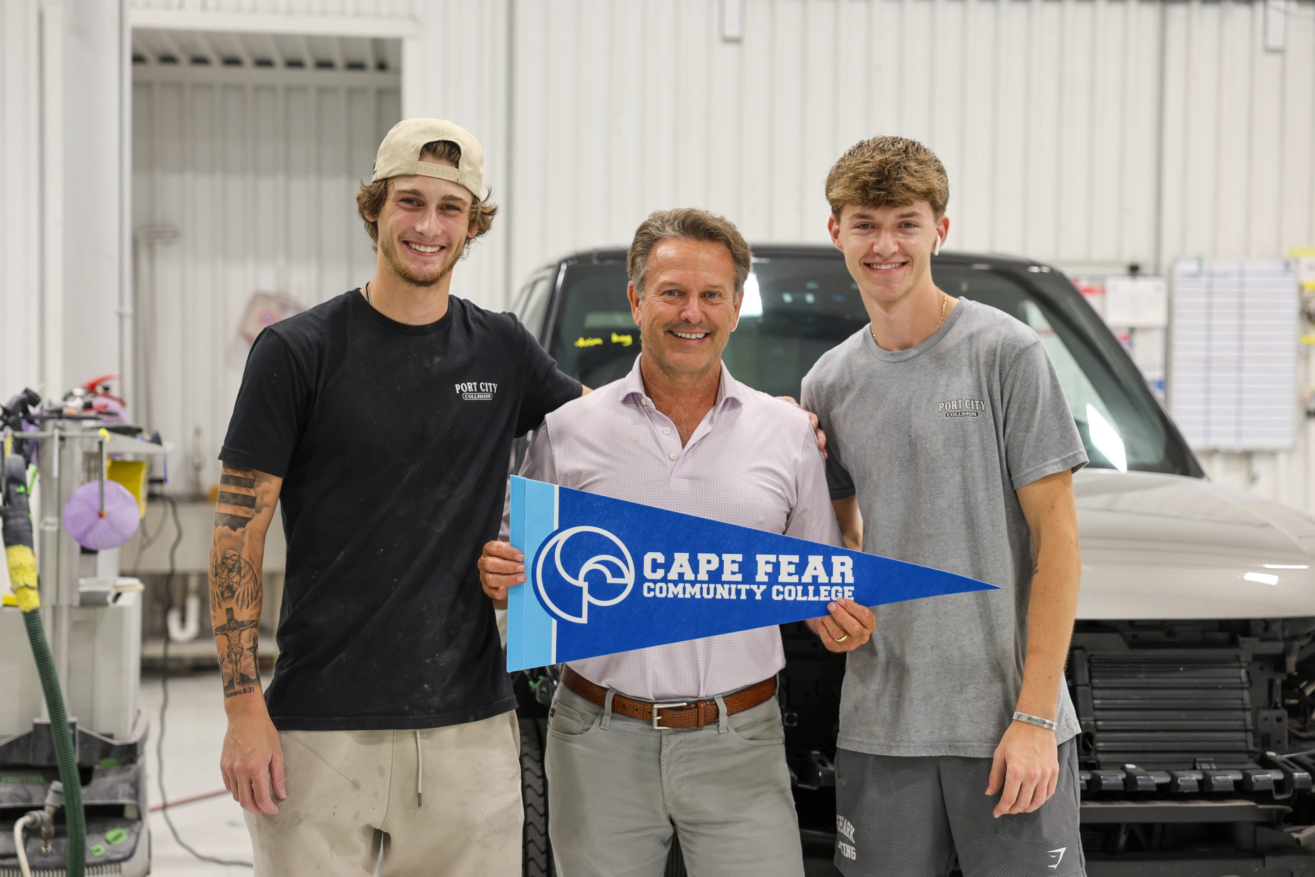 Three men smile inside an auto body shop