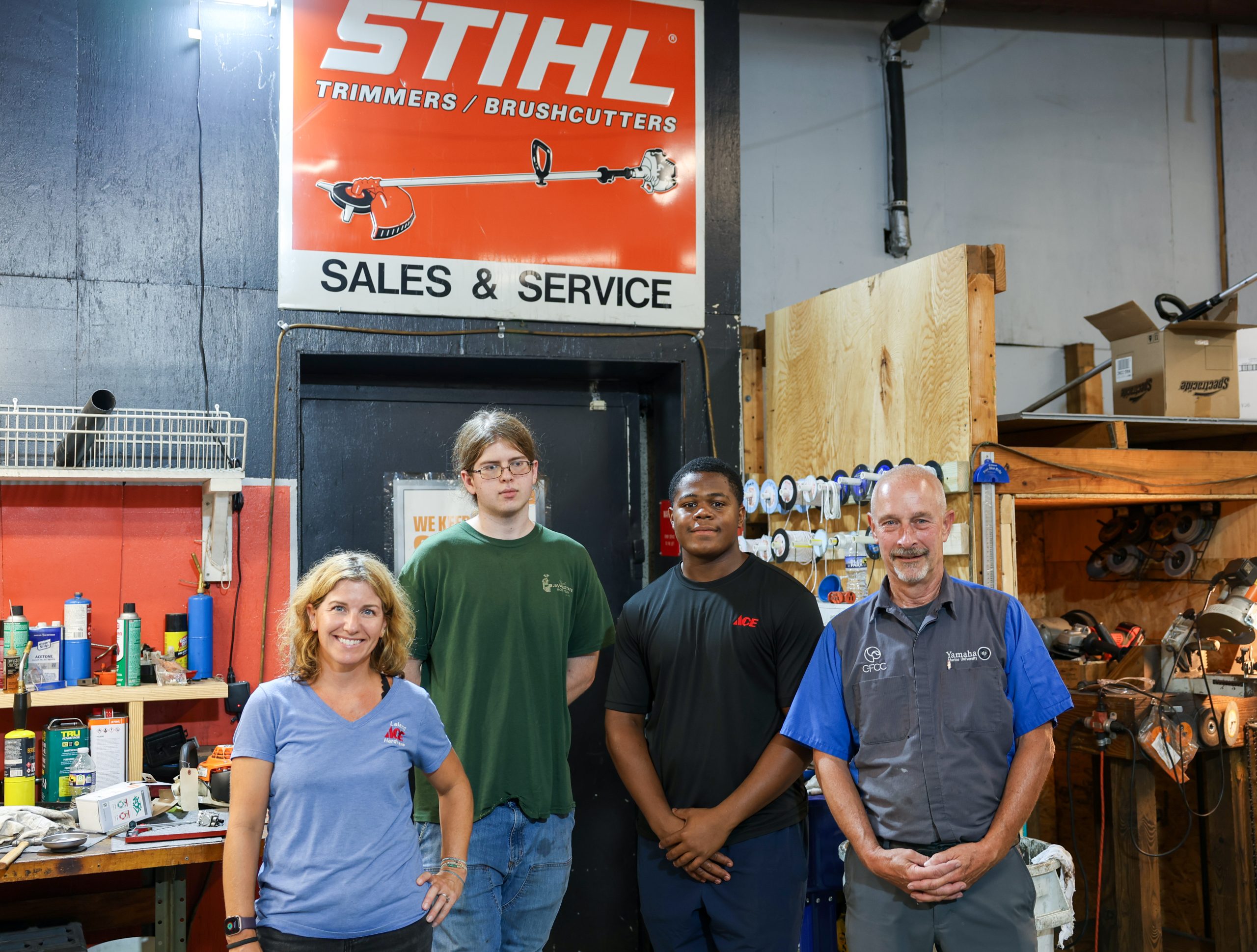 Four people stand inside a workshop beneath a STIHL sales and service sign.