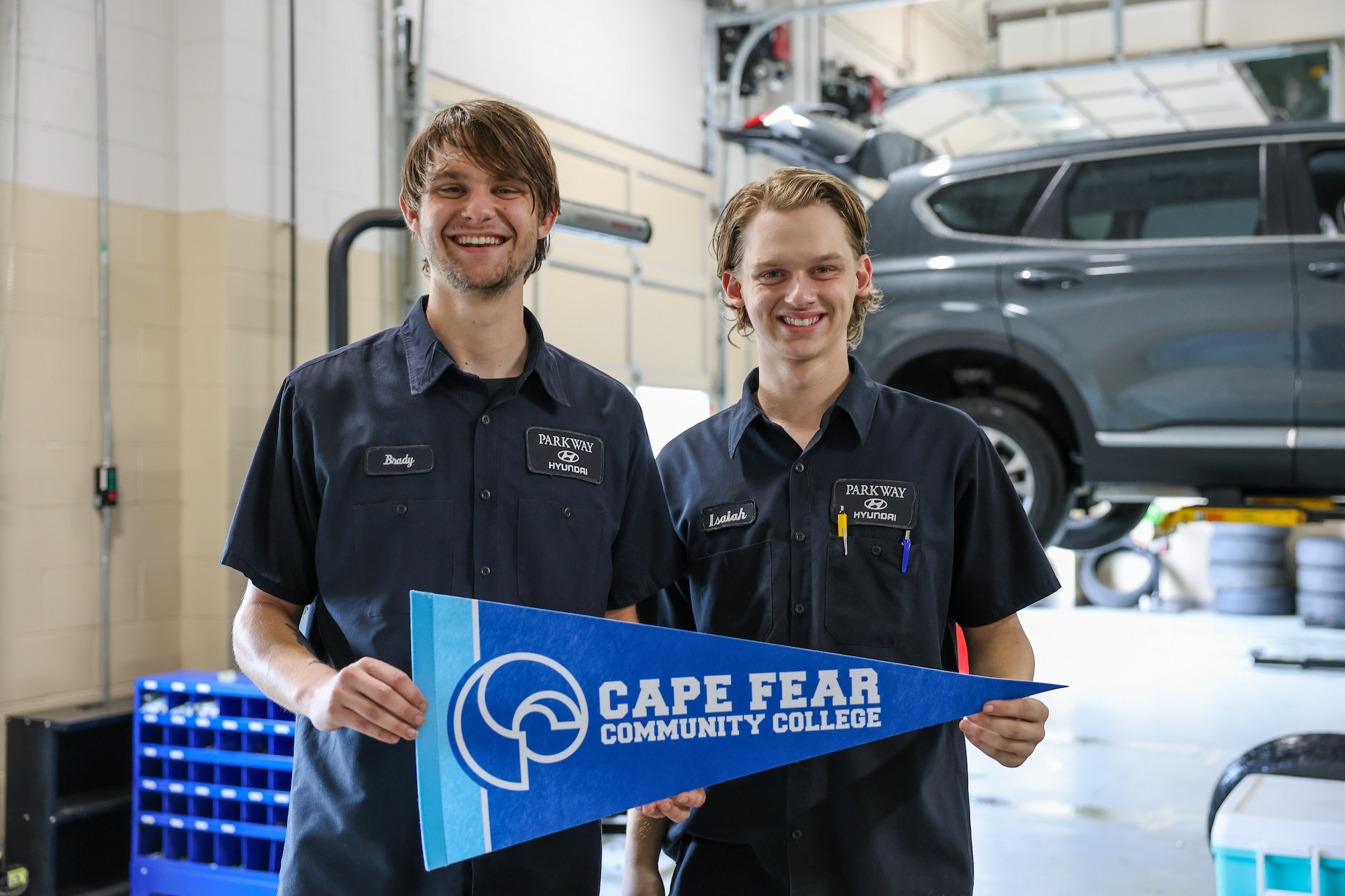 two techs in car shop holding cfcc flag