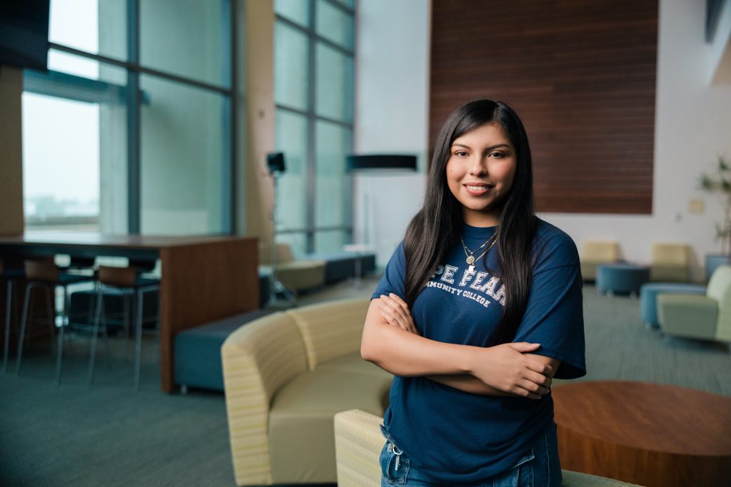 Girl standing in the lobby of an educational builing with arms cross wearing at Cape Fear Community College tee shirt.