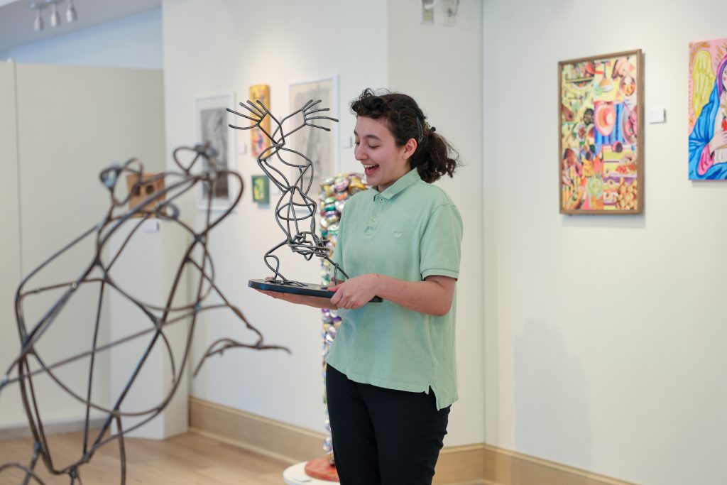 alumni holding her artwork speaking to audience at art gallery