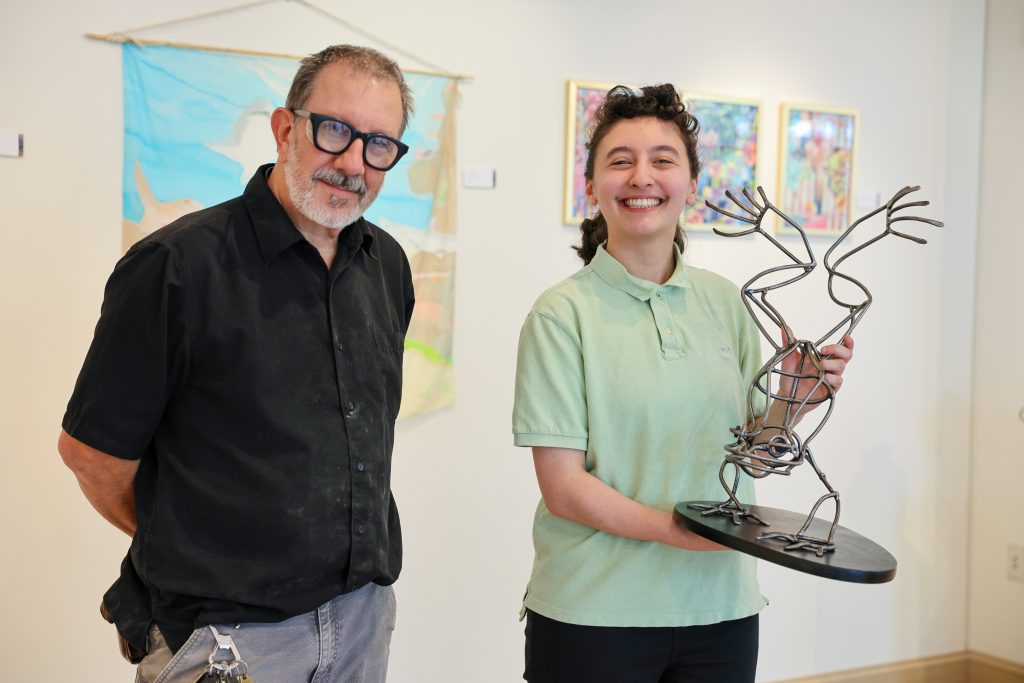 alumni stands with her artwork next to faculty member