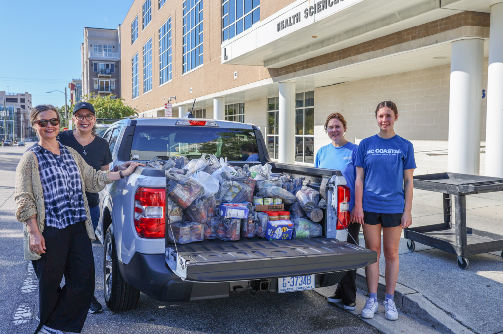 Photo of four women around a pickup truck full of food donation for a food pantry.