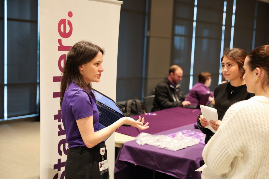Novant employee talks to two students at a healthcare hiring fair.