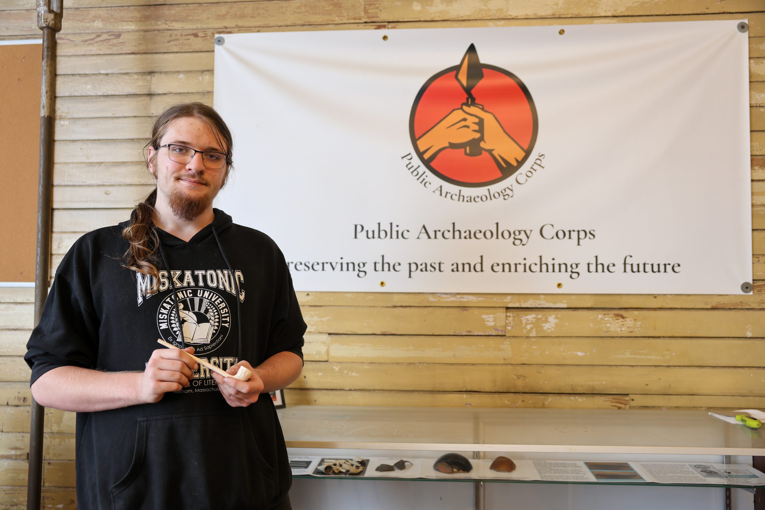 alex clupper in archaeology lab standing in front of sign