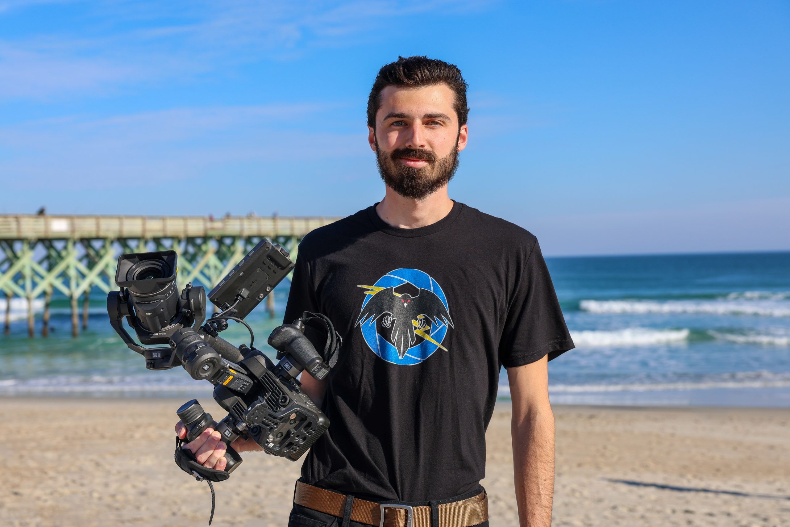 male standing on the beach posing with a camera in his hand