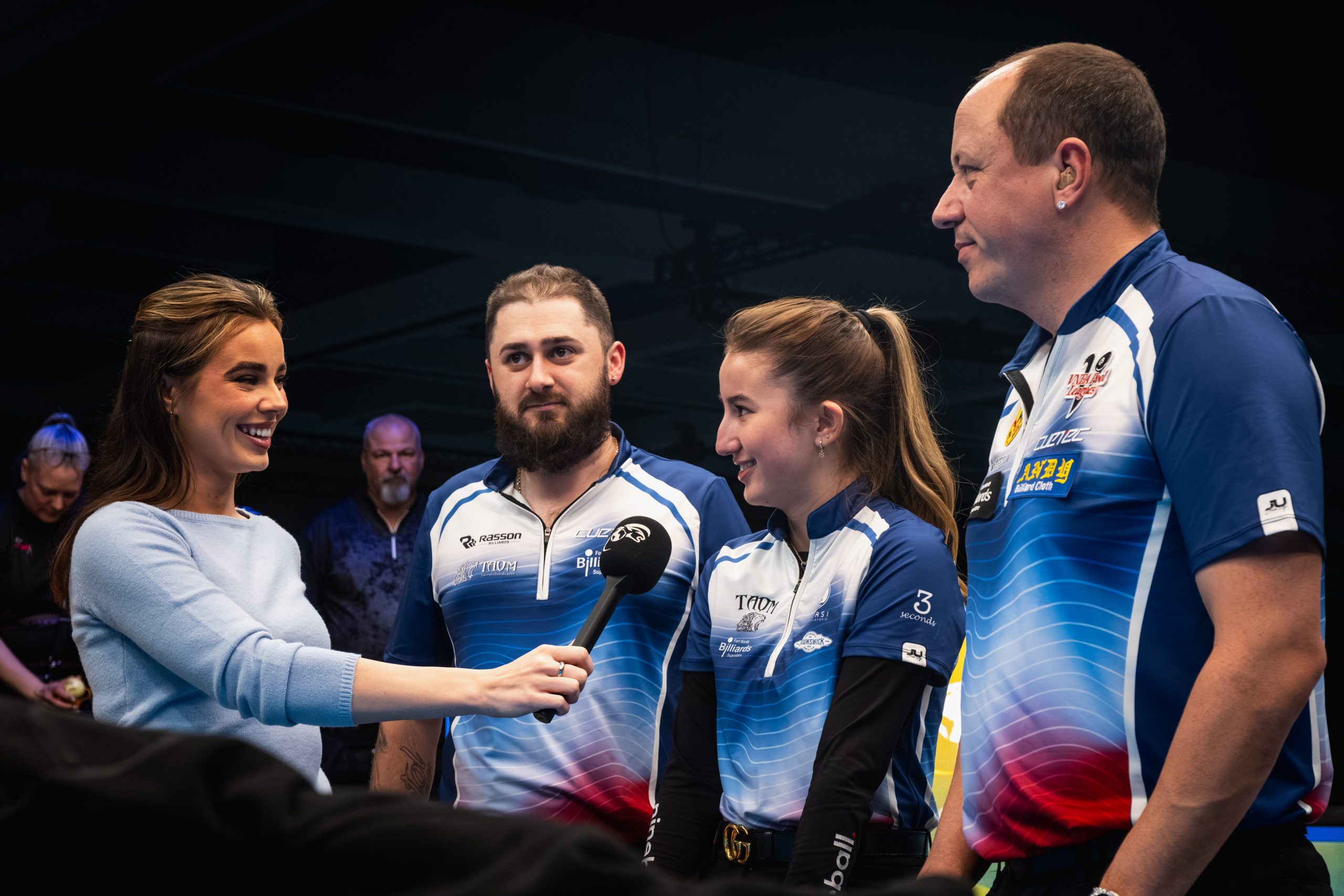 Reporter interviewing three billiards players beside a pool table.