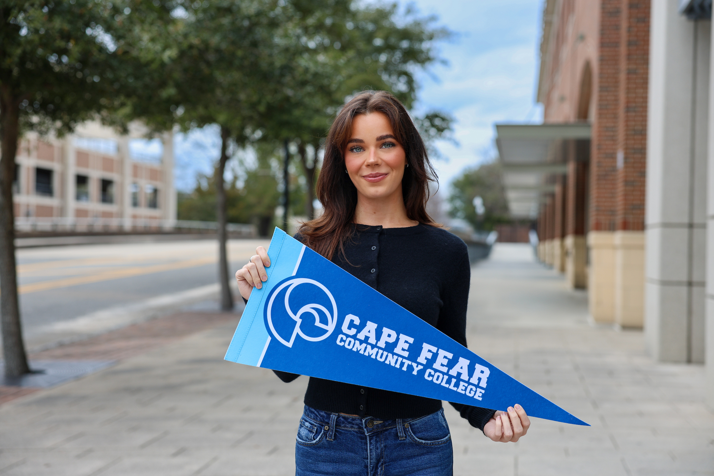female stands on campus holding a cape fear community college flag