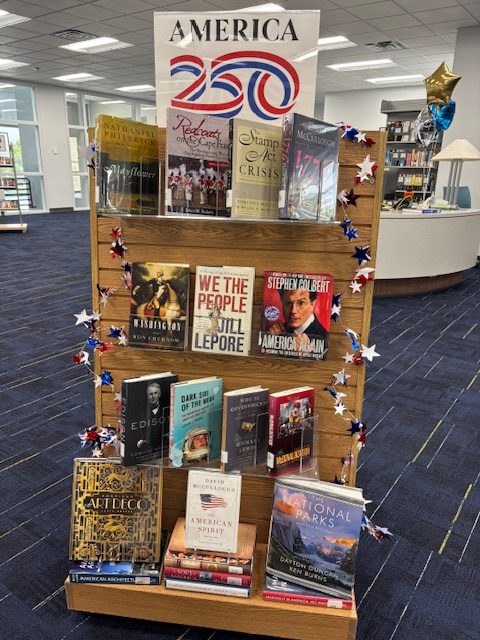 "AMERICA 250" book display in a library featuring American history titles decorated with patriotic star garland.