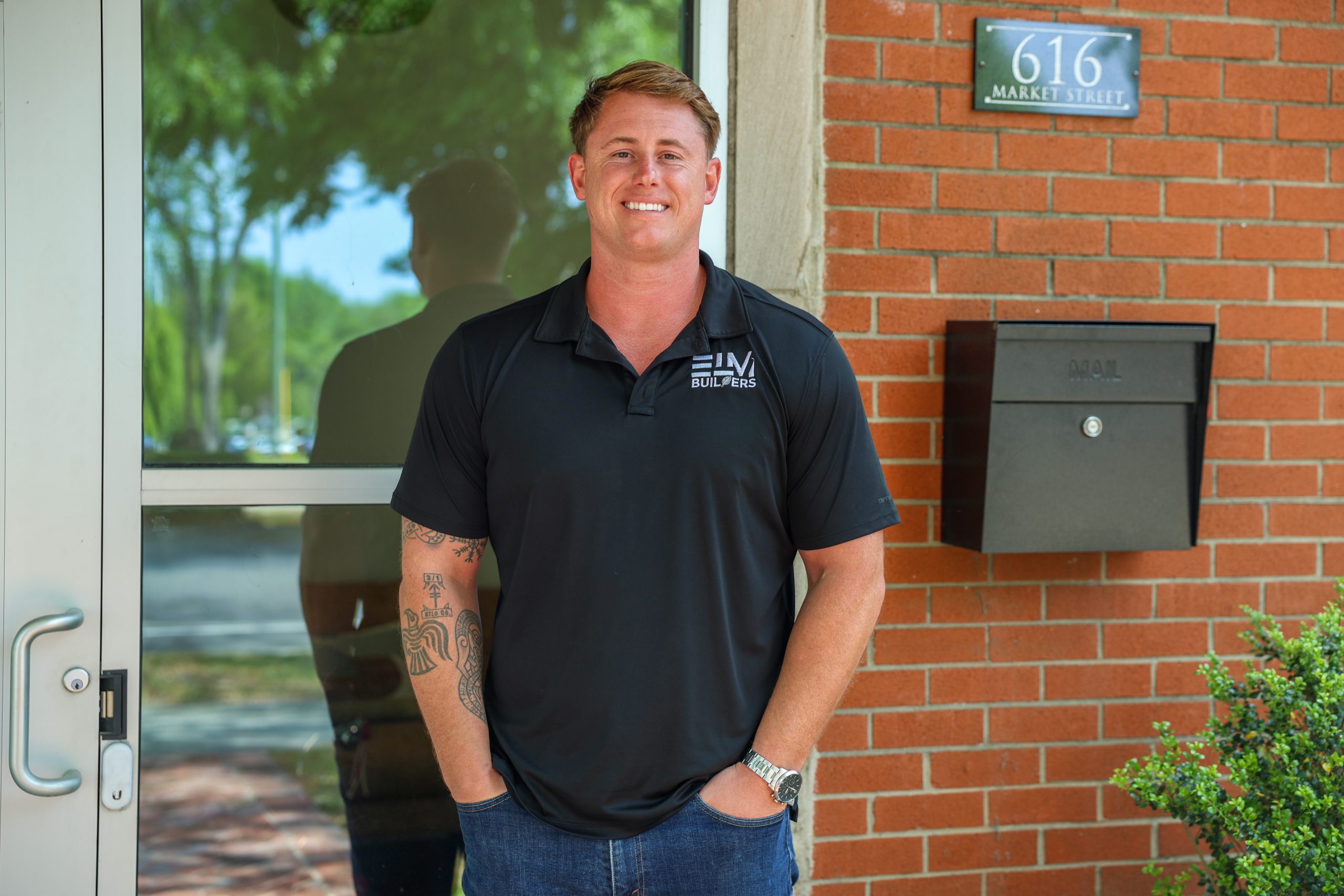 headshot of a man standing outside of brick building wearing an elm builders shirt