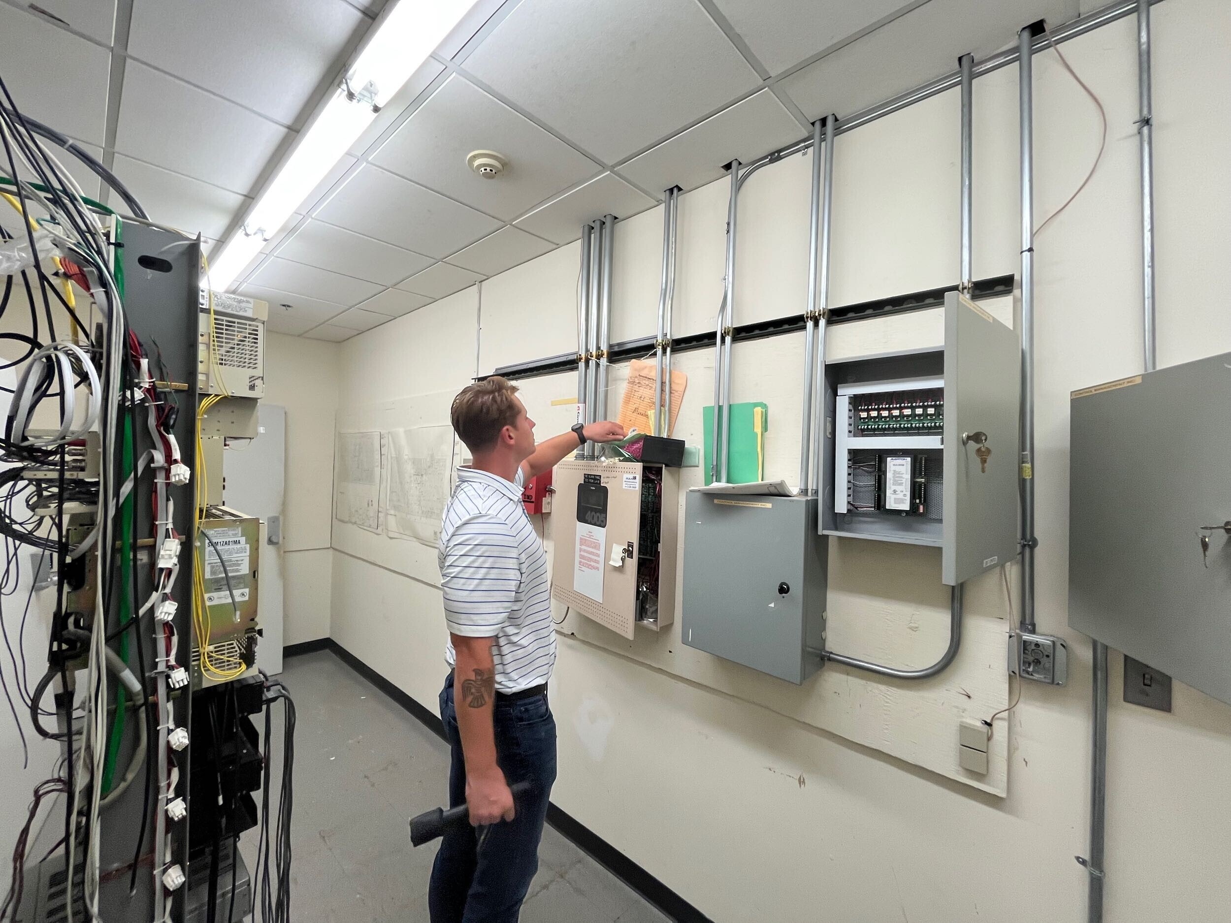 A person inspects electrical panels and wiring in a utility room.