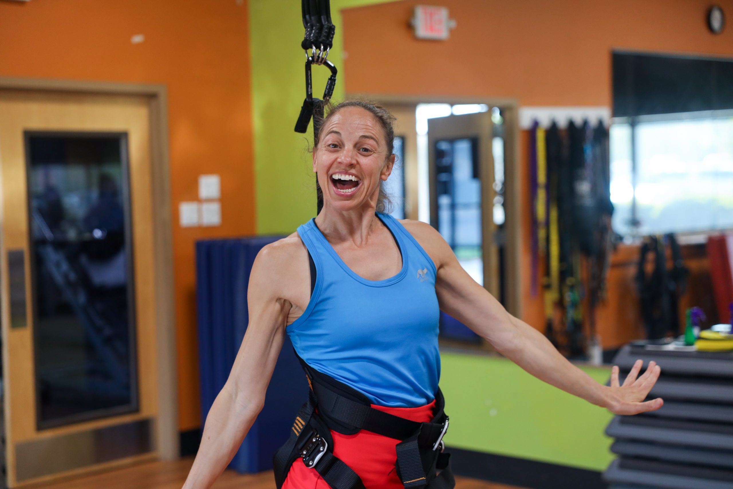 Woman smiling energetically while wearing a workout harness in a gym.