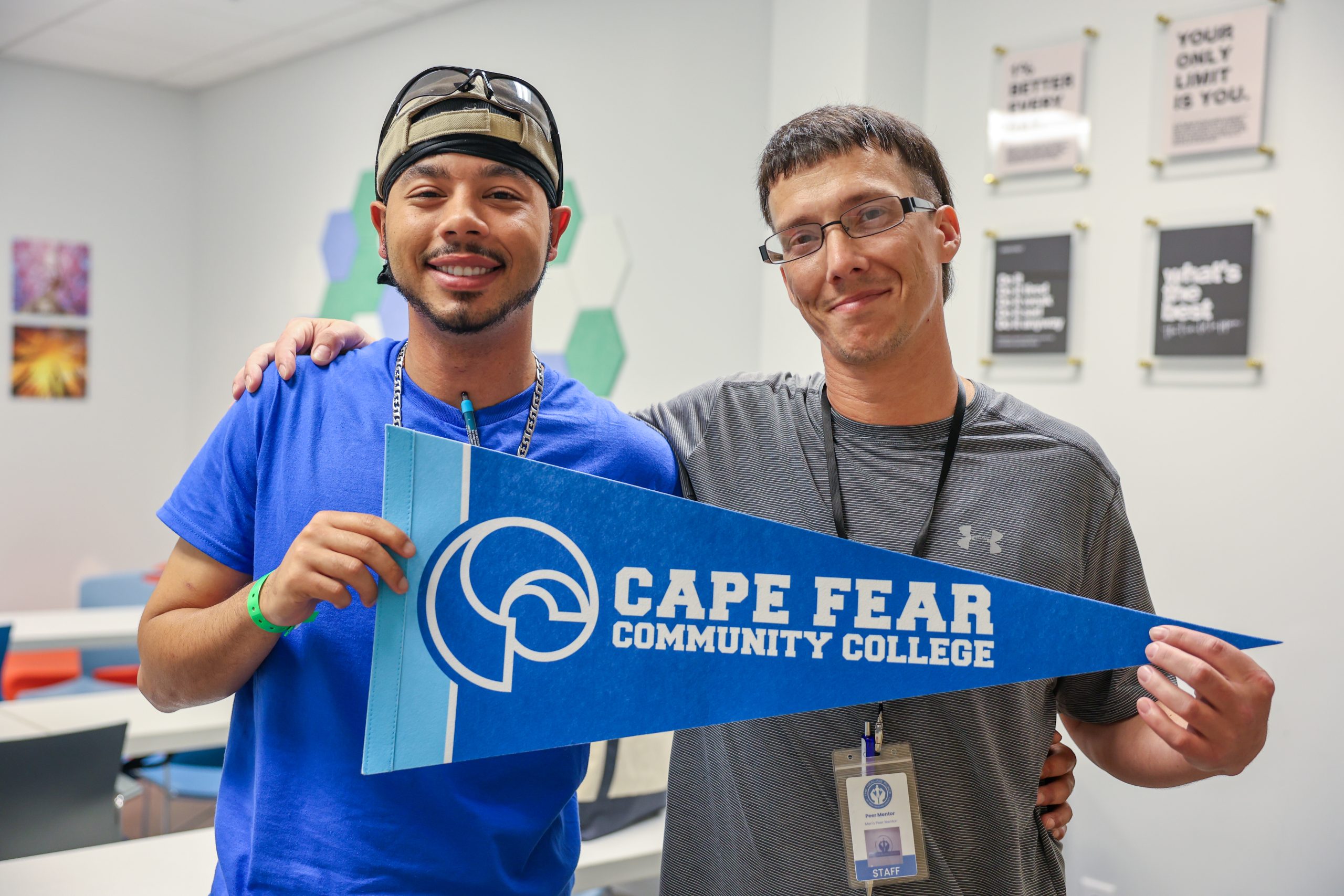 two men holding a cape fear community college pennant in a classroom