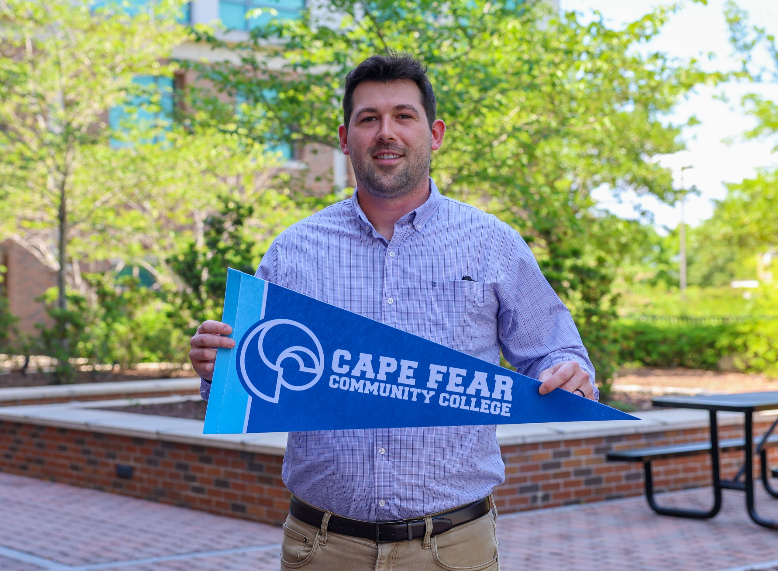 man holding cape fear community college pennant outside on college campus