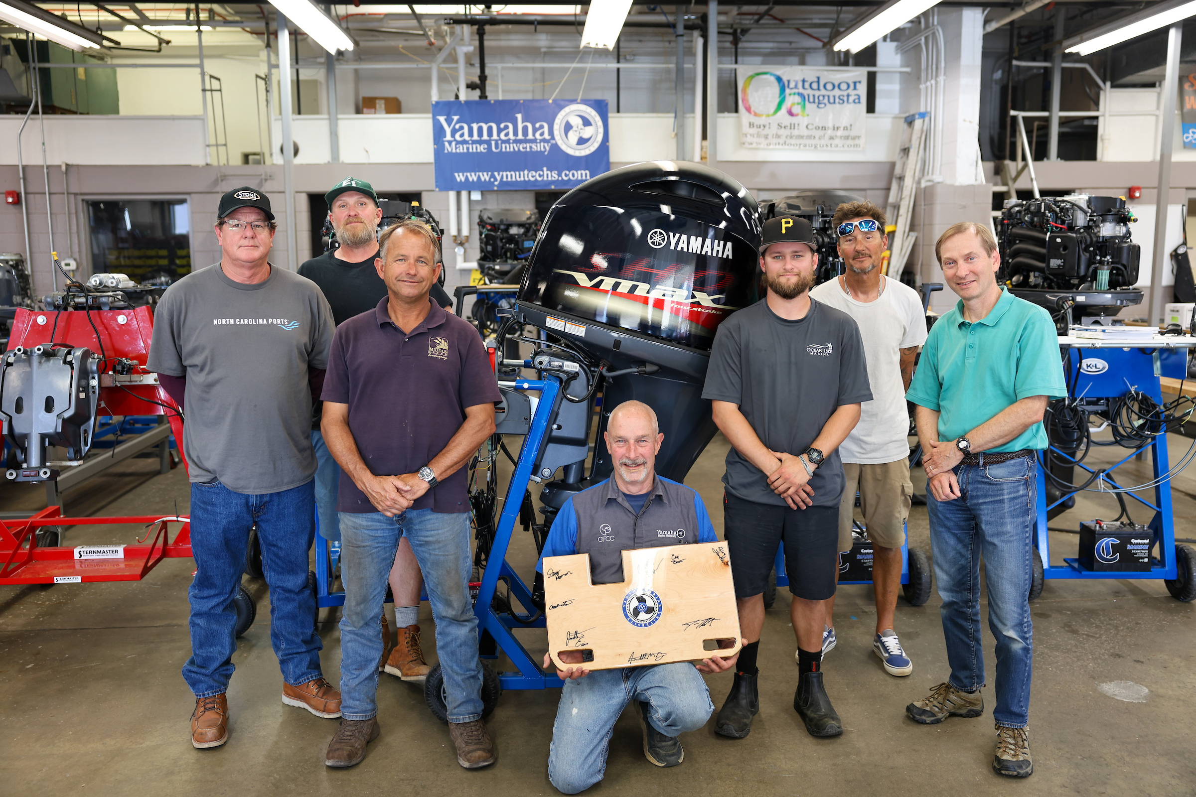 group of outboard system students huddled around their instructor holding a commemorative plaque