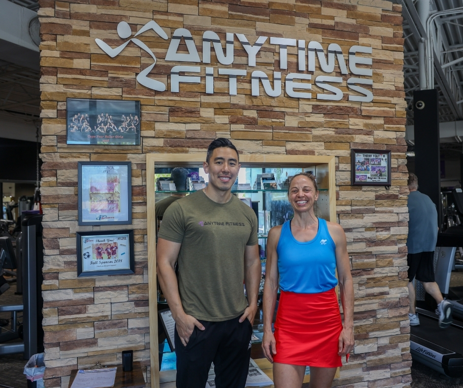 Two people smiling in front of an Anytime Fitness gym sign.