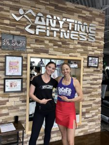 Two people smiling in front of an Anytime Fitness gym sign