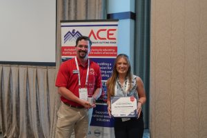 Two conference attendees stand in front of an America's Cutting Edge (ACE) display banner during an awards presentation. One person holds a recognition plaque while the other presents a trophy. The certificate recognizes Cape Fear Community College with the "Strongest Industry Buy-In" award. Both individuals are smiling and wearing conference name badges.