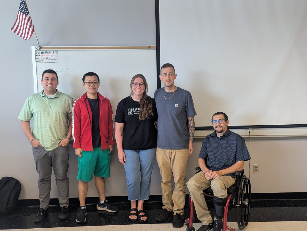 five individuals in a classroom setting smiling for camera