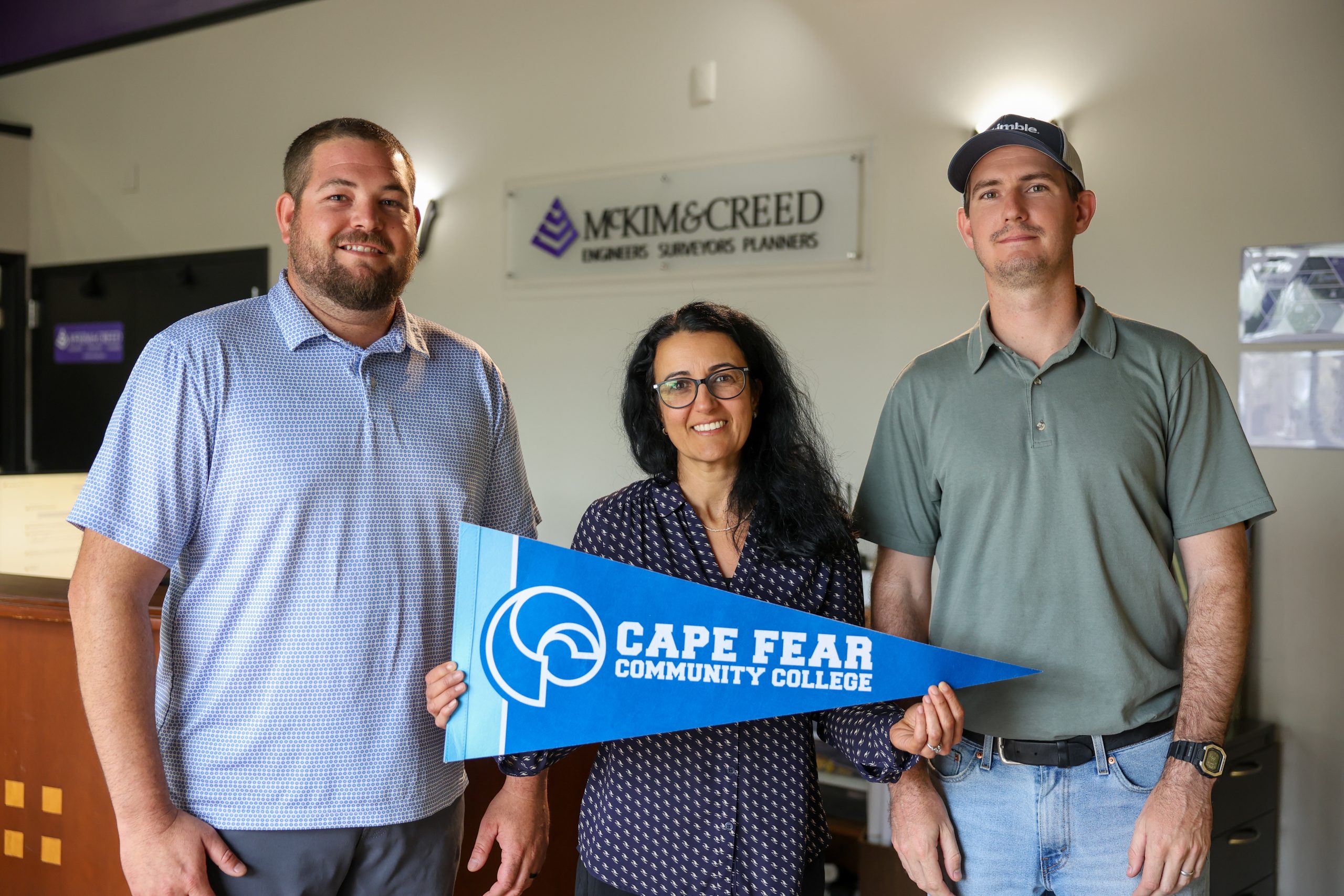 three colleagues stand in office setting holding cfcc flag