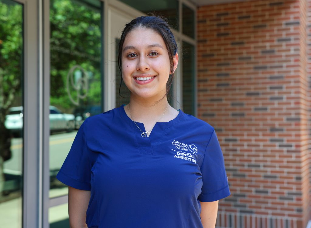 student wearing dental scrubs smiling for photo outside of building