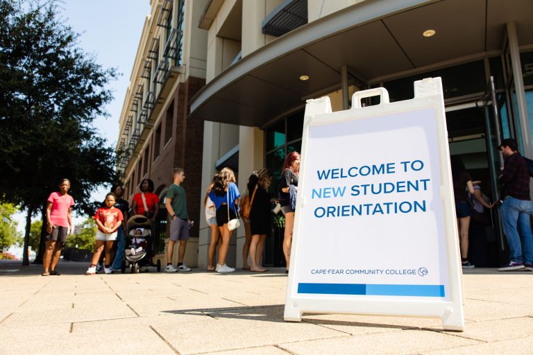 Cape Fear Community College new student orientation sign outside a campus building as students and families gather near the entrance.