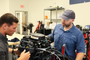 Instructor demonstrates an outboard boat engine to a student in a hands-on marine technology workshop.